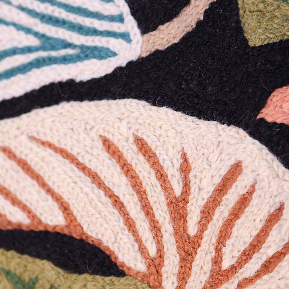 Close-up of a textured, raised-chain stitch embroidery with abstract organic shapes in cream, terracotta, teal, olive green, and black.