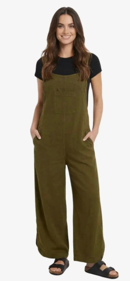 A woman modeling olive green wide-leg utility jumpsuit over a black t-shirt and black sandals, standing against a plain white background.